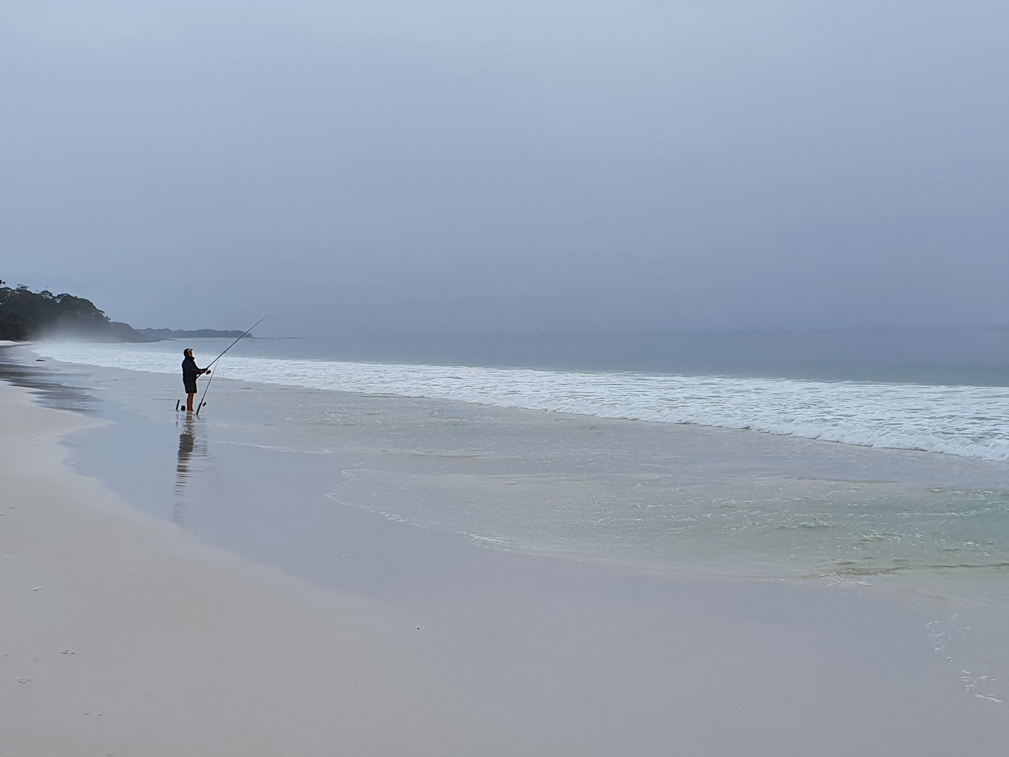 A man fishing on a rainy beach, capturing the essence of solitude and nature's beauty in beach photography.