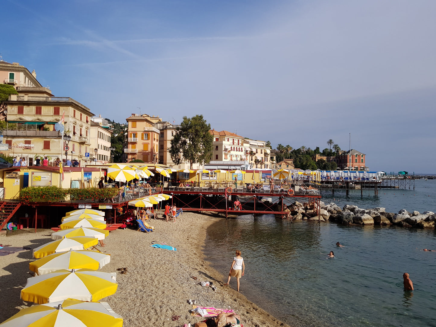 Capturing a sunny day on the Italian Riviera; the yellow striped umbrellas line the shore as people enjoy the calm, clear water.