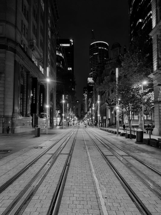 Beautiful black and white photo captured pre-dawn, the city lights glow above he tram lines of George St Sydney.
