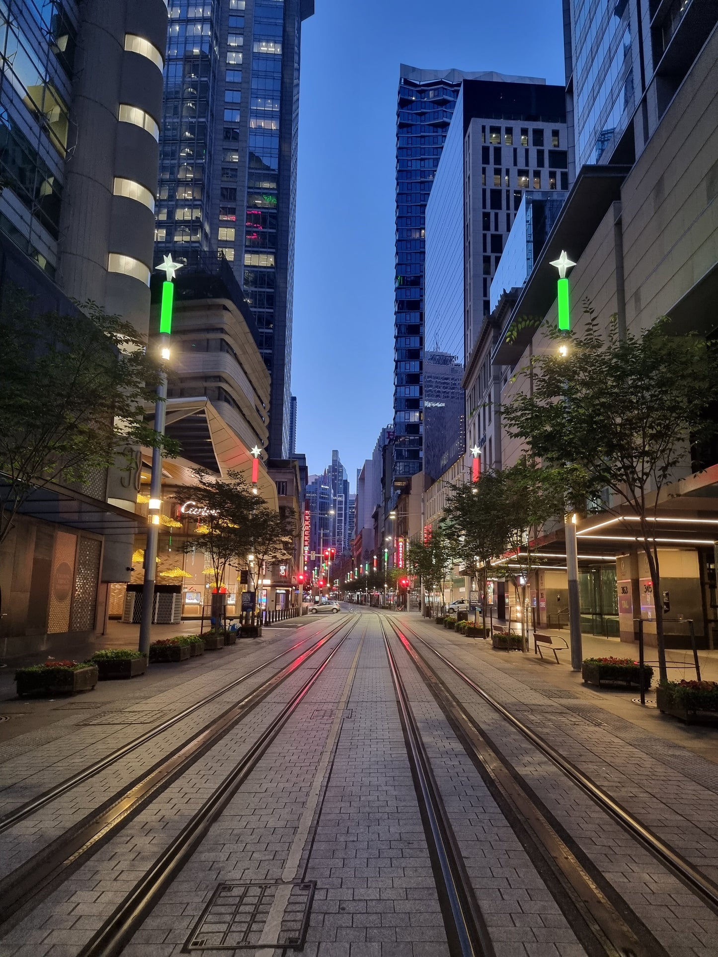 George St, Sydney photo, with the tram lines stretching into the distance of the city, lit by the neon lights of the towering buildings.