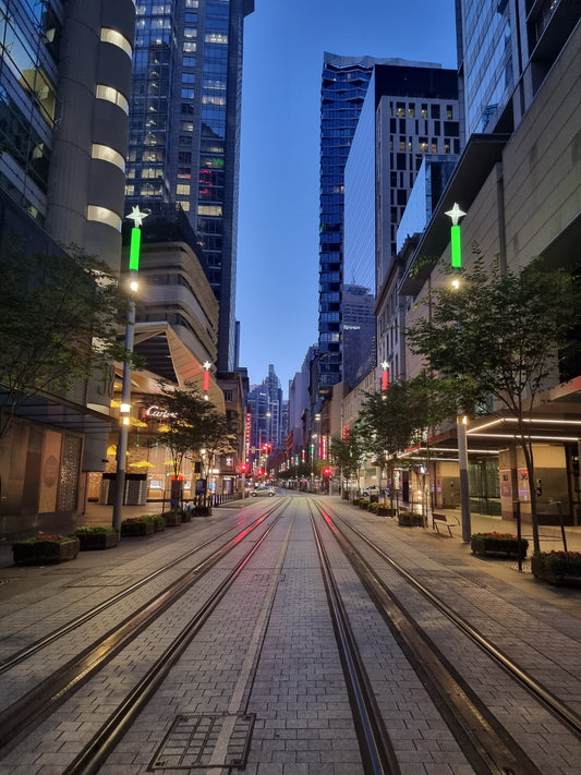 George St, Sydney photo, with the tram lines stretching into the distance of the city, lit by the neon lights of the towering buildings.