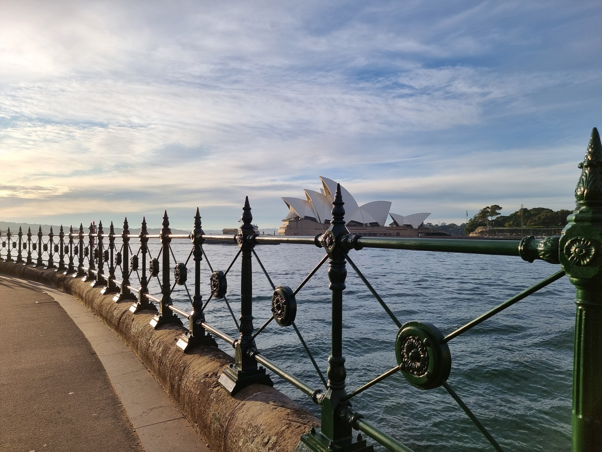 Viewed through the iron fencing cross Circular Quay, capturing the shell-like cluster of the Sydney Opera House.