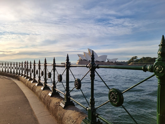 Viewed through the iron fencing cross Circular Quay, capturing the shell-like cluster of the Sydney Opera House.