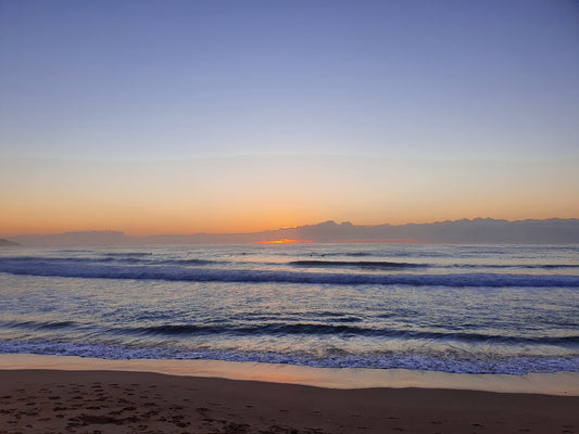 Pastel colours of dawn fill the sky and ocean, with white capped wave rolling to the shore.