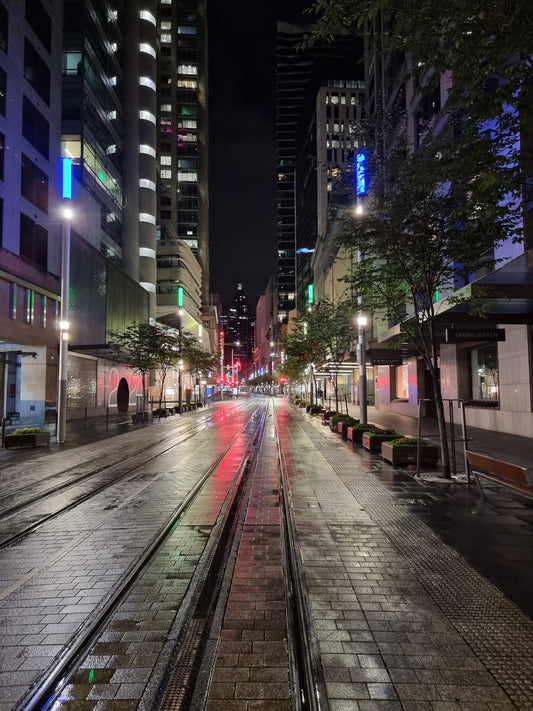 Early morning. The dark, wet street is lit with fluorescent reflections cast from the buildings' neon lights.